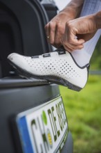 A person puts on white cycling shoes on the trunk of a car ready for the ride, triathlon, Calw,