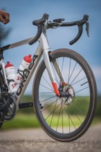 Front view of a racing bike with two water bottles standing on a country road under blue sky,