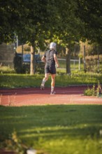 A jogger runs on a red track in the countryside, surrounded by trees on a sunny day, triathlon,
