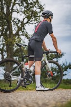Cyclist leaning against a bicycle, resting on an outdoor trail, triathlon, Calw, Germany
