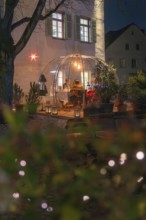An illuminated outdoor dome at night with people eating, surrounded by plants and lights, Gastro