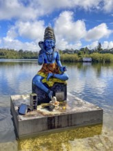 Statue sculpture of deity Shiva on the shore of stands in sacred Hindu lake Ganga Talao at