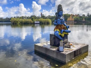 In the foreground statue sculpture of the deity Shiva stands in sacred Hindu lake Ganga Talao at