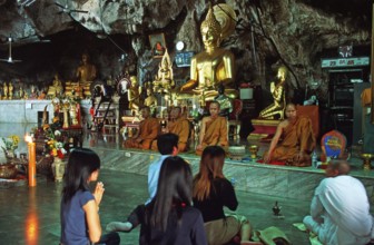 Buddha statue, monks and believers praying, Wat Tam Sua monastery near Krabi, Thailand, December
