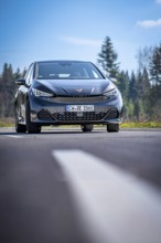 Modern black car on a country road in front of a forest under a blue sky, electric car Cupra, e-car
