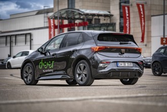 A Cupra car in a municipal parking lot with modern architecture in the background, seen from the