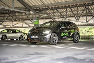 A dark car is parked under a roof in a modern parking garage, electric car Cupra, e-car sharing,