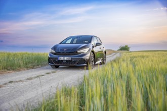 A Cupra drives along a rural path surrounded by fields and an impressive sunset in the background,