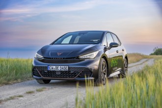 Car on a dirt road with beautiful fields and blue sky in the evening light, electric car Cupra,