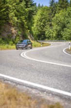 Black car on winding country road along green forests in sunny ambiance, Cupra electric car, e-car