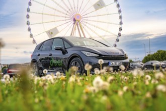 Car on a green field with a Ferris wheel in the background, electric car Cupra, e-car sharing,