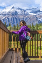 Female hiker standing on a wooden viewpoint, admiring the breathtaking scenery of mount robson, the
