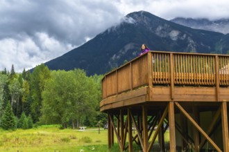 Tourist standing on a wooden deck, admiring the breathtaking view of mount robson, the highest peak
