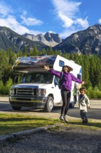 Happy mother and son are jumping in front of their recreational vehicle near mount robson in the