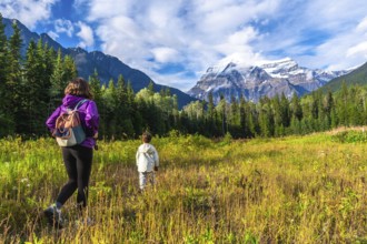 Hikers are enjoying a scenic walk through a meadow with majestic mount robson towering in the