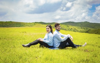 Couple in love in the field sitting back to back looking at the the camera, Young relaxed couple