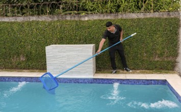 Swimming pool cleaning and maintenance concept. Maintenance person cleaning a swimming pool with