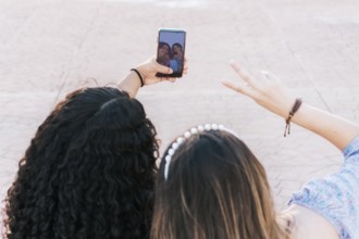 Two smiling teenage girl friends taking a selfie and pointing fingers up. Close up of two smiling