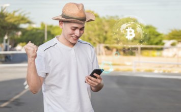 Man using smart phone with bitcoin symbol floating on screen, man checking cell phone with bitcoin