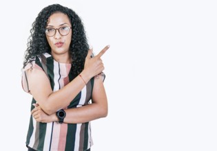 Beautiful afro young woman pointing an advertising to side. Surprised girl in glasses pointing to a