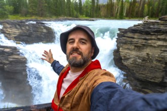 Happy tourist taking a selfie with powerful athabasca falls cascading into a narrow gorge in the