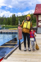 Mother and son holding paddles and wearing life jackets, getting ready for a canoe trip on the