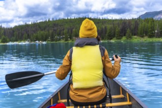 Tourist wearing yellow life jacket and beanie paddling a canoe in maligne lake, jasper national