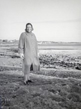 Full length portrait of smiling woman wearing winter coat and clothing standing by seaside, Devon,