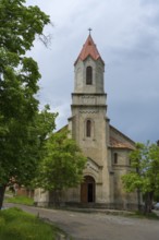 Large church with Gothic bell tower and red roof tiles surrounded by green trees, German