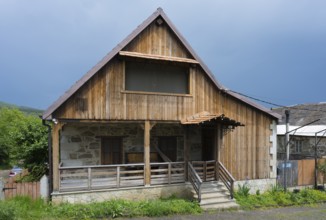 Rustic wooden house with veranda on a rural road under a cloudy sky, Schwabenstraße 25, village