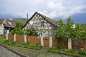 Half-timbered house with wooden fence and satellite dish, surrounded by green trees under cloudy