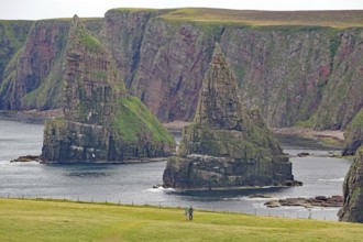 Cliffs with distinctive rock formations and two hikers in the foreground, Duncansby Stacks, John O'