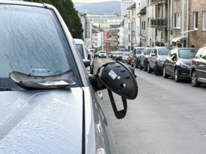A car on the side of a steep residential street. The vehicle's left wing mirror is severely damaged