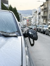 A car on the side of a steep residential street. The vehicle's left wing mirror is severely damaged