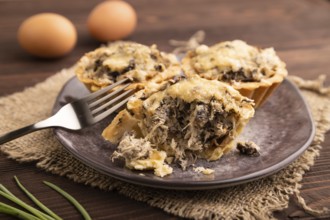 Tartlets with meat and cheese on brown wooden background and linen textile. side view, close up,