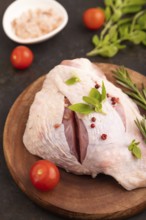 Raw Turkey Thigh with spices and rosemary on cutting board on black concrete background and linen