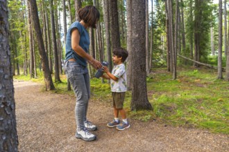 Mother hands a water bottle to her son during a hike on a sunny day surrounded by the lush green
