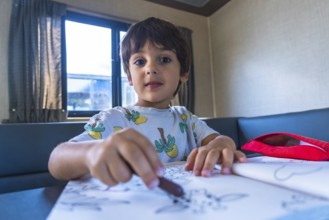 Young boy concentrating on drawing with crayons in a camper van, enjoying creative activities
