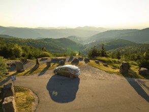 Car parked at a viewing point with a wide view over a mountainous forest area at sunset, deer e-car