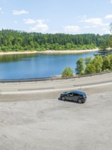 A car on a winding track with a view of a lake and forest in the background, deer e-car sharing,