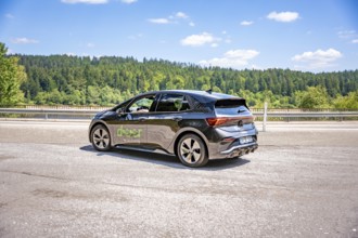 Black car on a country road against a background of green forest and blue sky, deer e-car sharing,