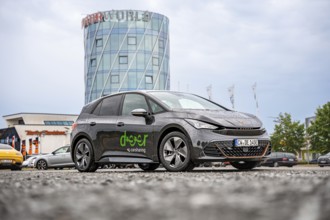 Car next to a modern tower and shopping center, deer e-car sharing, Cupra electric car, Motorworld.