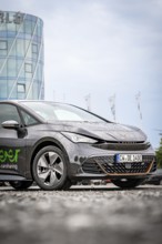 A rain-wet car in front of a modern office building, Deer E-Car Sharing, Cupra electric car,