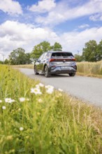 Black car driving on a country road with blooming meadows and cloudy sky, deer e-car sharing, Cupra