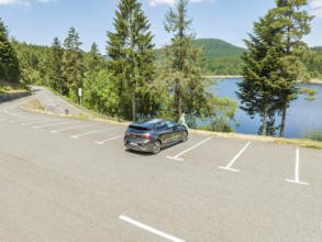 A car is parked near a lake, surrounded by forest and mountains on a clear day, deer e-car sharing,
