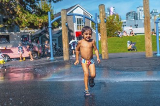 Happy child is running through water jets at a playground in vancouver, british columbia, on a