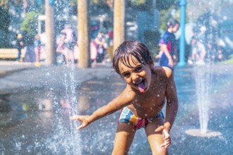 Happy child sticking out his tongue while playing in a water fountain on a sunny day in vancouver,