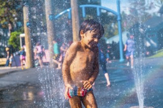 Happy muddy child playing and enjoying a refreshing spray in a water fountain at a playground in