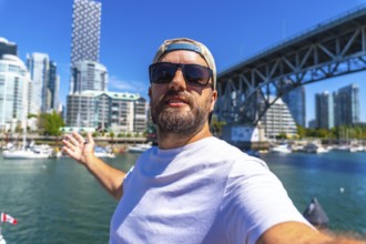 Happy man taking selfie with outstretched arm showing vancouver skyline, cambie street bridge and