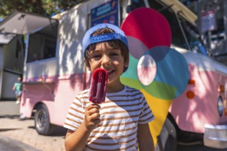 Smiling boy enjoying a refreshing popsicle on a sunny day, standing near a colorful food truck in